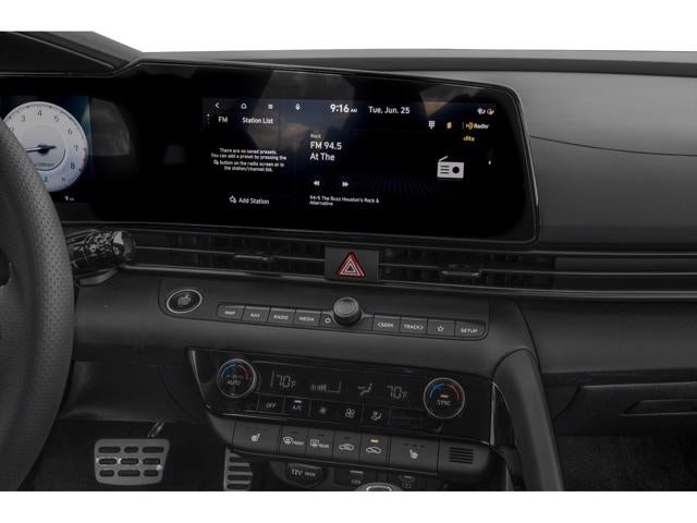 The dashboard of a vehicle, showing the infotainment screen displaying current radio station information and media controls.