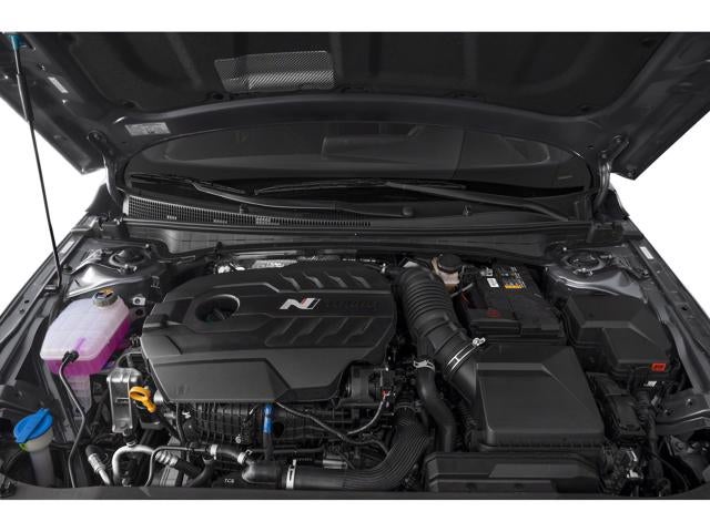 A car's engine compartment, with the hood open, revealing a black engine and various car parts.