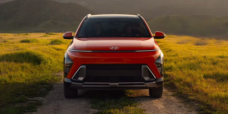A bright orange Hyundai Caspar SUV on a dirt road in a field of tall grass with mountains in the background.