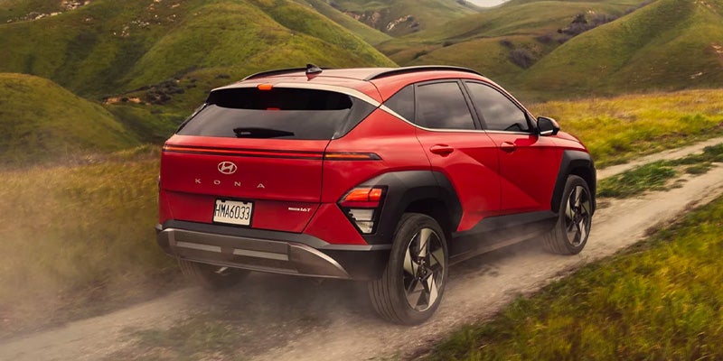 Red Hyundai Kona N Line driving on a dusty dirt road through green hills.