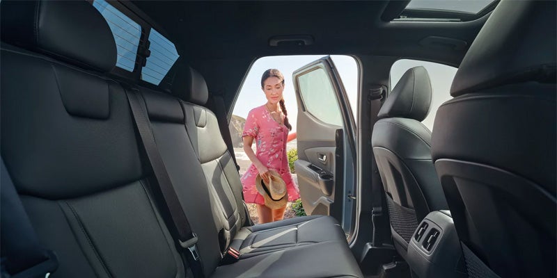 Interior shot of a car, showing black leather seats leading to a woman in a pink dress getting in.