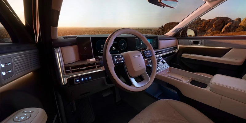 The view from the driver's seat of a luxury car interior, with a beige steering wheel and desert landscape.