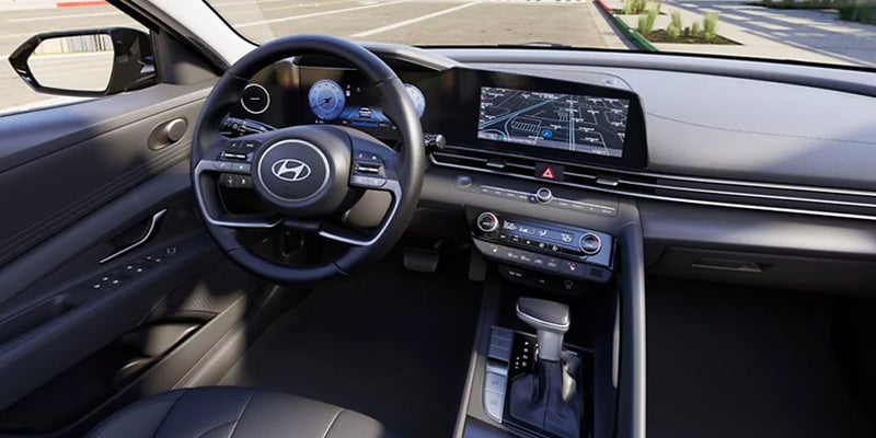 Interior shot of a car dashboard and steering wheel, with a digital display showing a map and a touchscreen infotainment system.