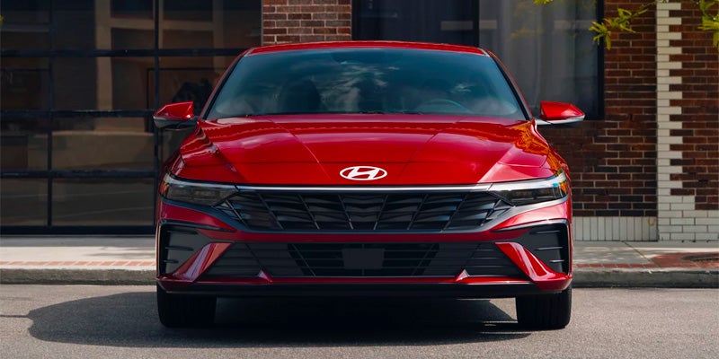 Front view of a sleek, red Hyundai sedan on a street in front of a brick building.