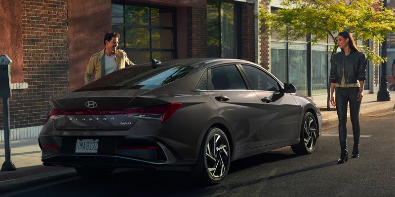 Dark gray Hyundai Elantra parked on a city street, with a man and woman walking toward it.