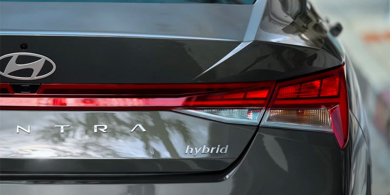 Close-up of the rear of a dark gray Hyundai Elantra Hybrid, showing the logo, taillights, and "hybrid" badge.