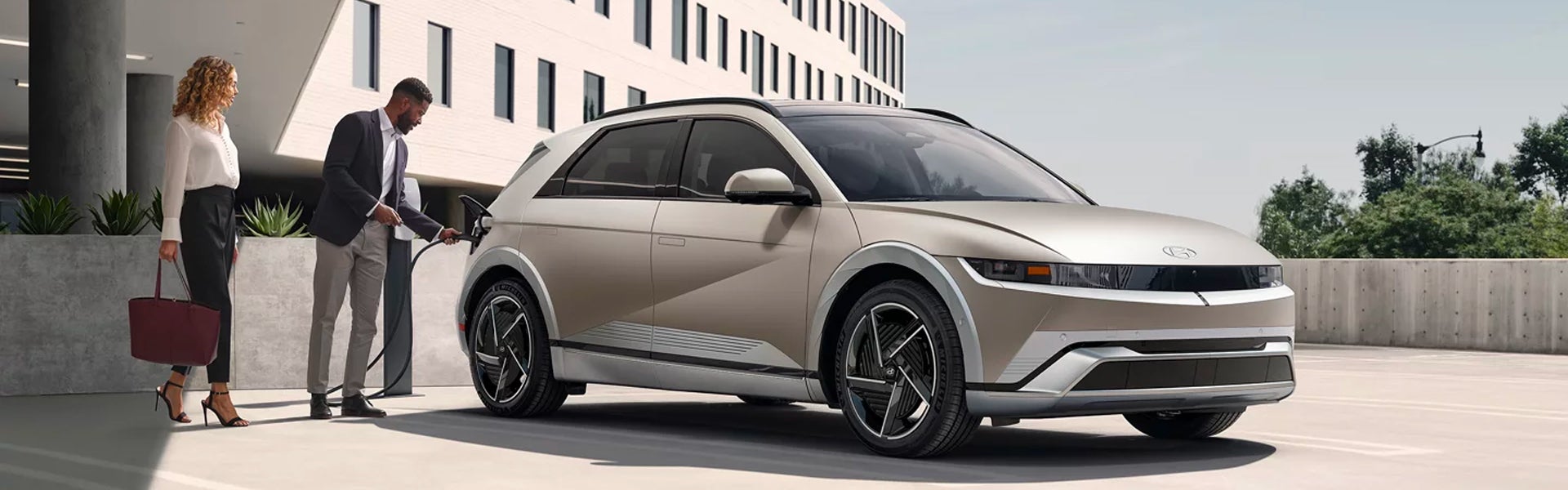 A man charges a beige Hyundai Ioniq 5 electric car while a woman watches