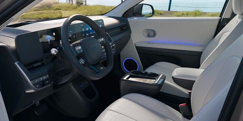 Interior view of a modern car with a light-colored cabin, dark dashboard, and blue accent lighting.