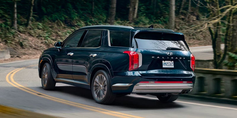 Dark blue Hyundai Palisade SUV drives away on a winding road through a forest.