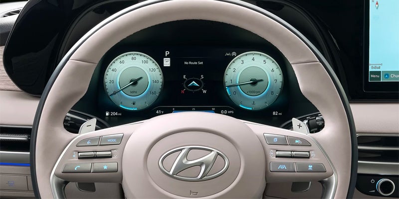 View from driver's seat of car dashboard showing cream steering wheel, digital speedometer, and tachometer.