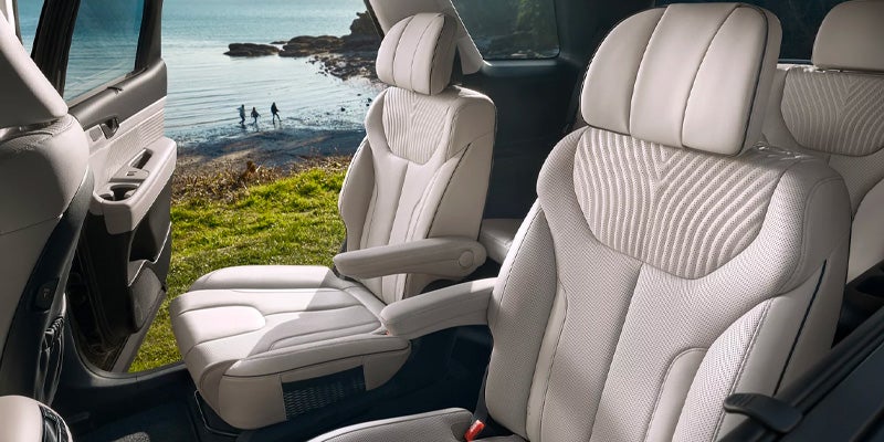 Car interior with light-colored, quilted leather seats and two individuals walking on a beach visible through the door.
