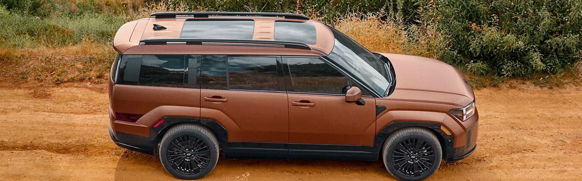 Top-down medium shot of a copper SUV with a dark roof rack and two sunroofs on a dirt road.