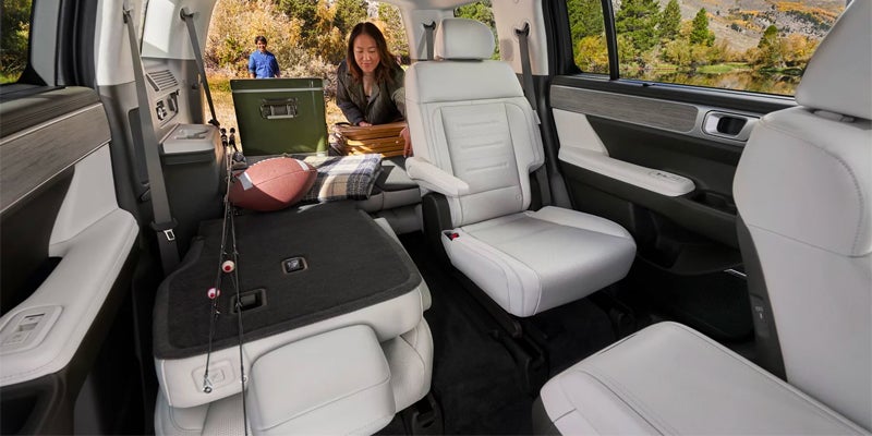 Interior of a car with a woman folding down seats for cargo space, a cooler and camping gear visible.