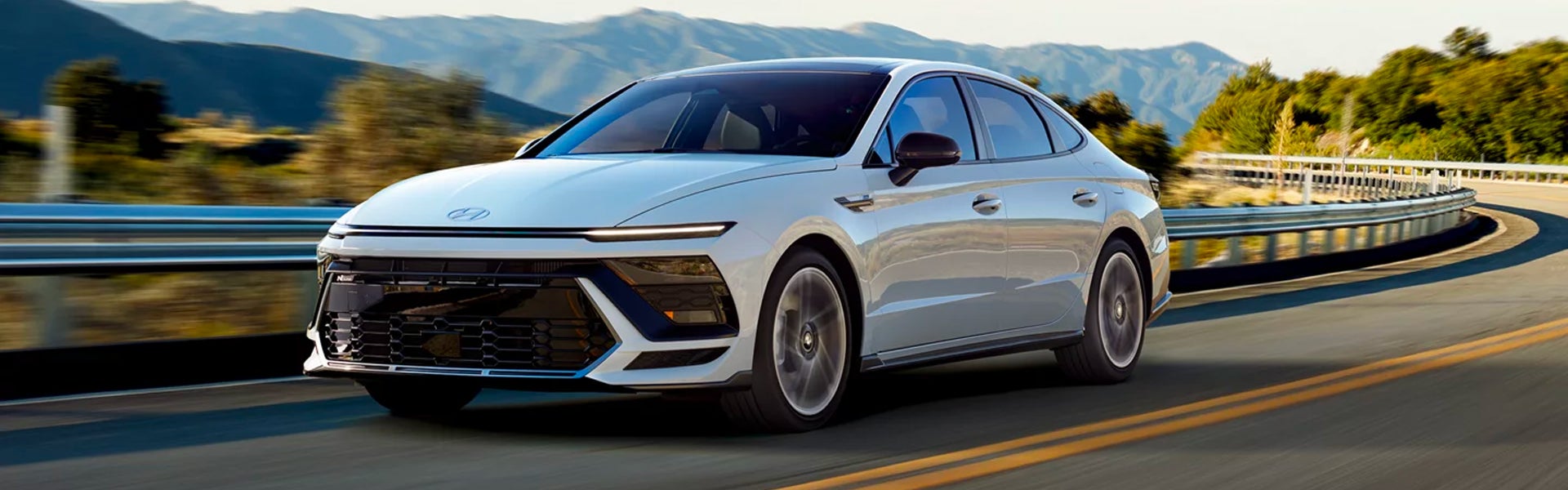Silver Hyundai car driving on a mountain road with guardrails.