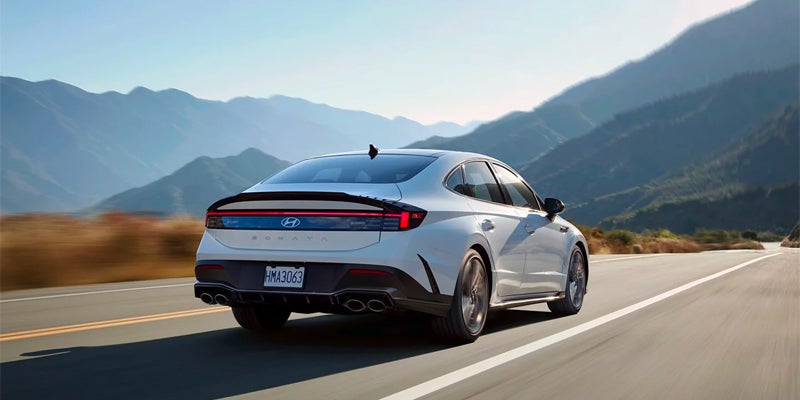 Rear view of a white Hyundai Sonata driving fast on an open road with mountains in the background.
