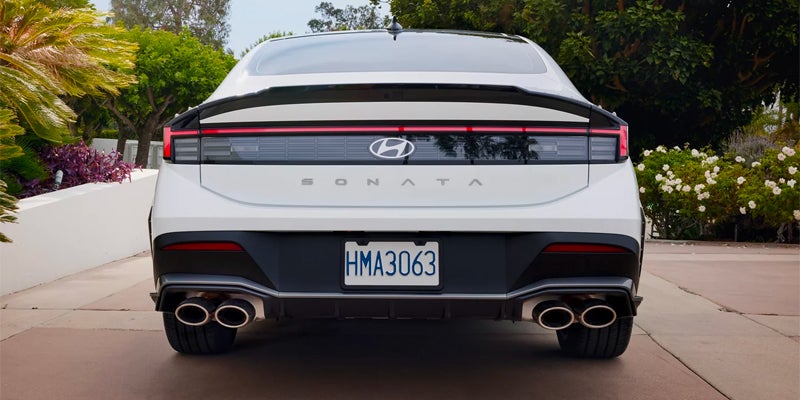Rear view of a white Hyundai Sonata sedan, featuring quad exhaust pipes and a full-width LED taillight.