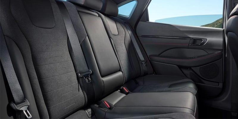 Rear interior of a car with dark leather and fabric seats, light blue sky visible through windows.