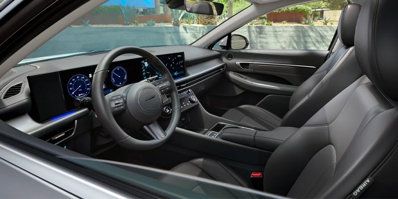 Interior view of a modern car cabin, showing the dashboard with digital displays, steering wheel, and black leather seats.