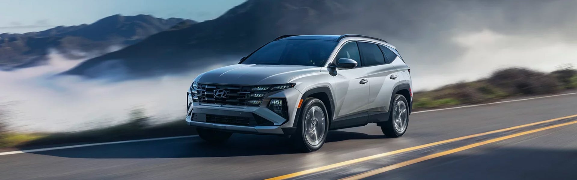 Silver Hyundai Tucson SUV driving on an open road with mountains and mist in the background.