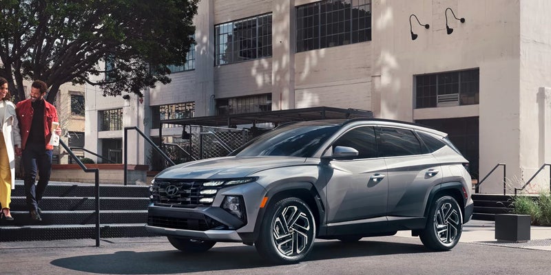 Silver SUV parked on a city street, with two people walking down stairs in the background.