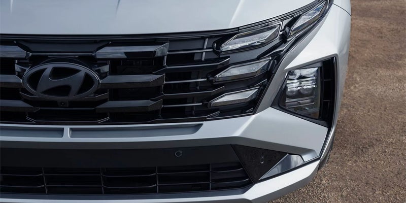 A dark gray Hyundai logo on a black grille with intricate lighting elements on a silver car.