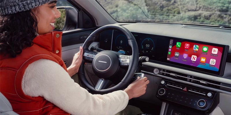 Woman in a red vest driving a car with a large touchscreen displaying smartphone apps like Apple CarPlay.