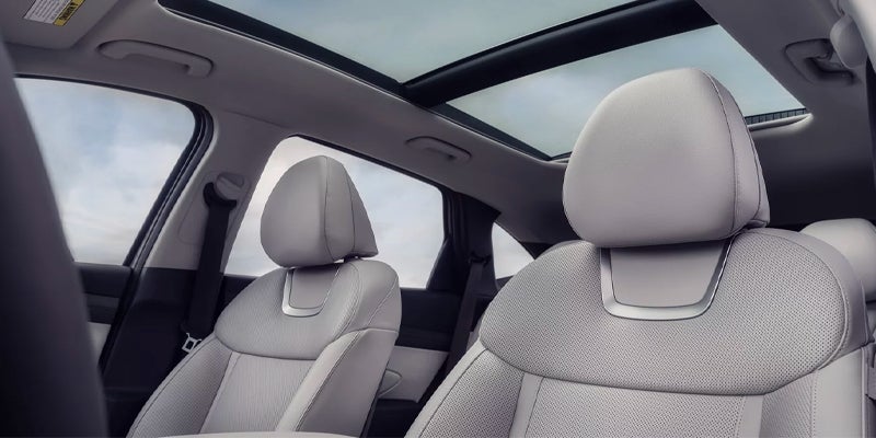 Interior view of a light gray car with a panoramic sunroof, showing two front seats with seatbelts.