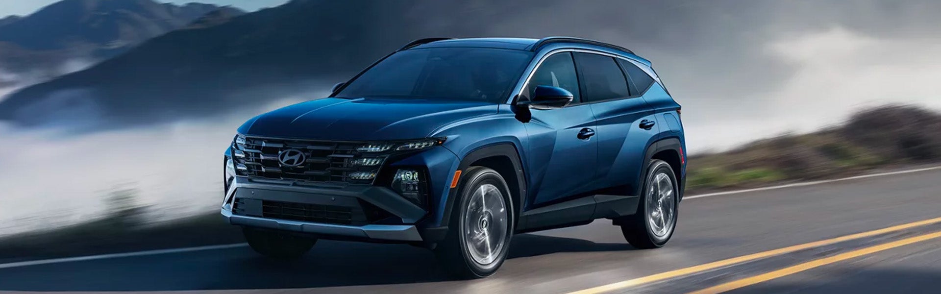A dark blue SUV driving on a highway with mountains in the background.