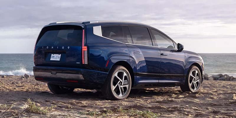 Rear view of a dark blue Hyundai Ioniq 7 electric SUV parked on a sandy beach at dusk.