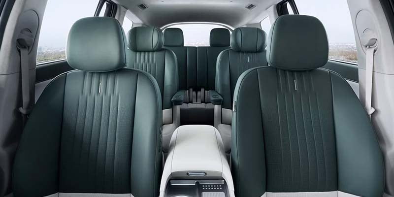 Interior of a vehicle featuring black leather seating, a console with controls, and two rows of visible seats.
