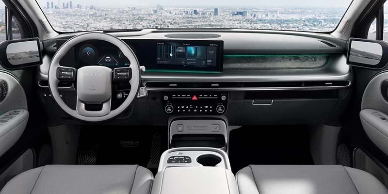 Interior of a modern car with a light gray steering wheel, digital displays, and a panoramic city view.