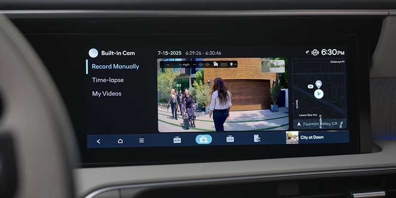 A car's infotainment screen showing a security camera view of several women outside a modern home, with a side menu and map.
