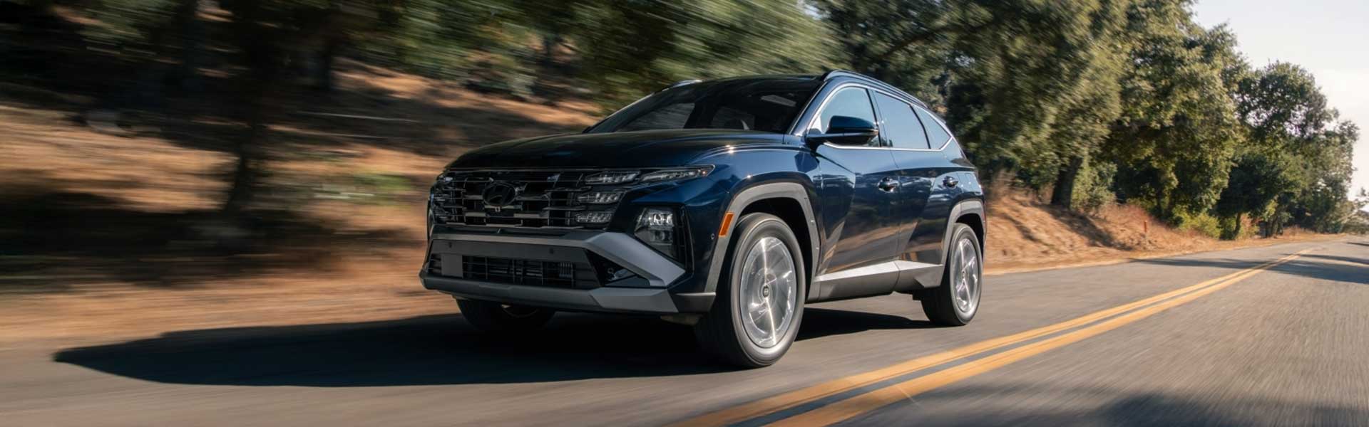 Dark blue Hyundai Tucson SUV driving on a road with blurred background trees, conveying motion.