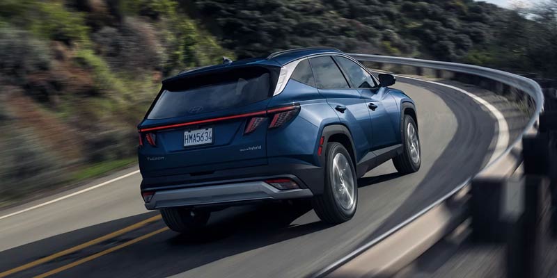 Rear view of a blue Hyundai Tucson driving on a curved road, with blurred motion suggesting speed.